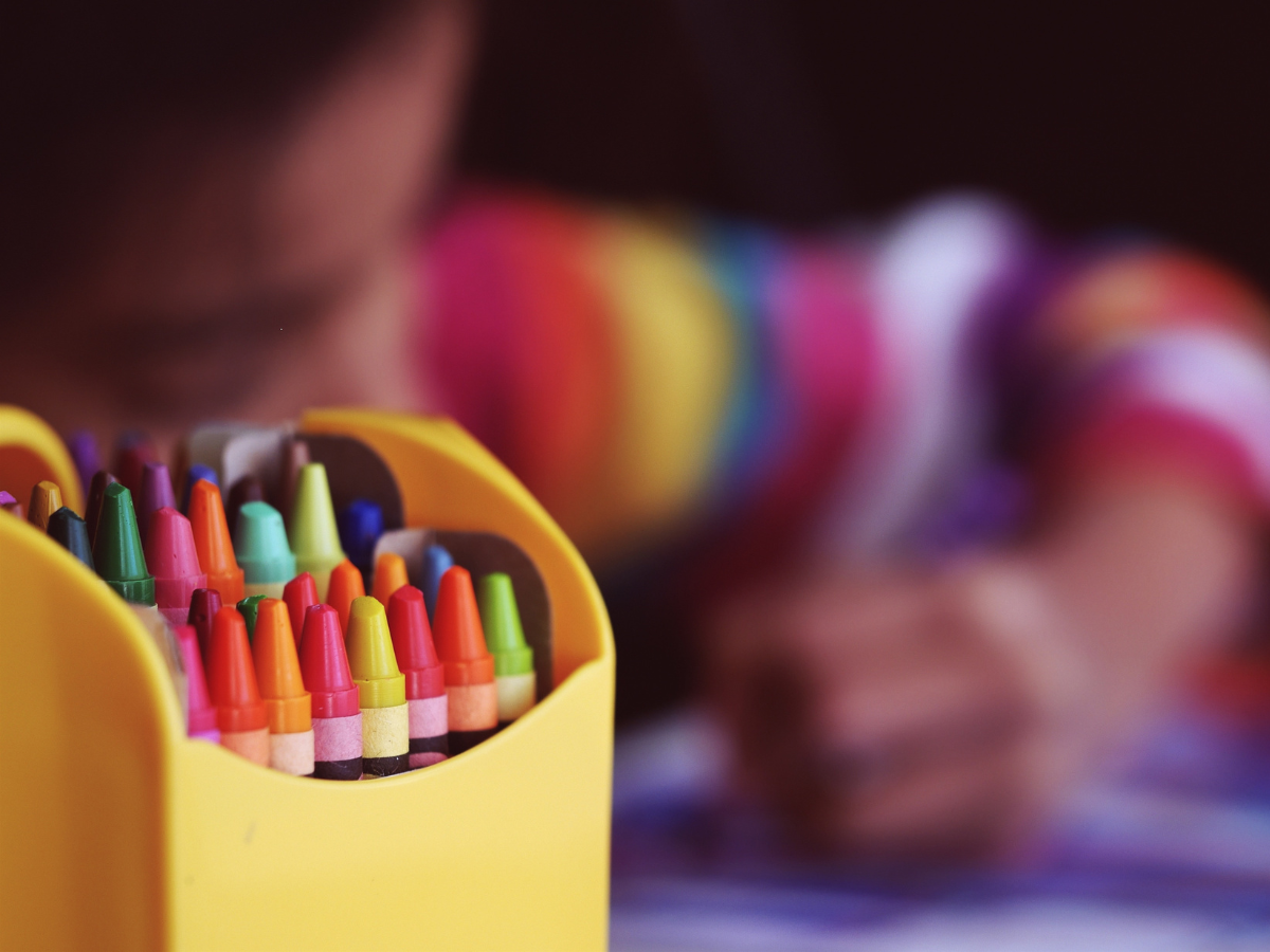 a box of crayons with a child coloring in the background