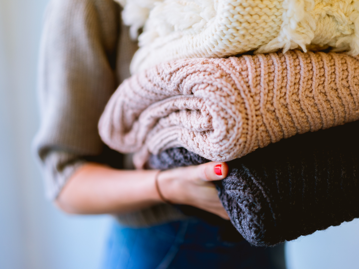 a woman holding three sweaters