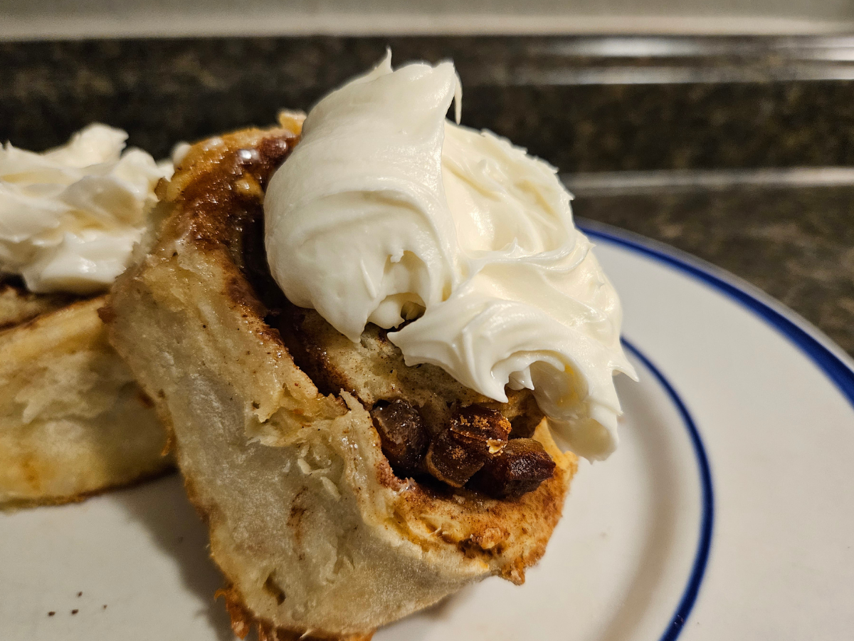 date and walnut stuffed sourdough cinnamon rolls topped with goat cheese icing on a white and blue plate